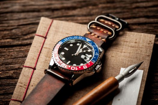 closeup luxury wristwatch for men with black dial blue-red bezel and leather strap.