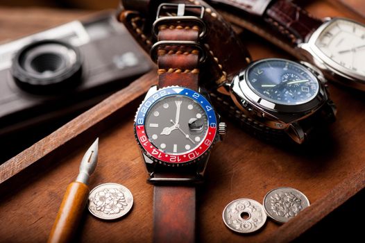 closeup luxury wristwatch for men with black dial blue-red bezel and leather strap. wristwatch with vintage men's objects.