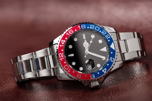 closeup luxury wristwatch for men with black dial blue-red bezel and stainless steel bracelet.