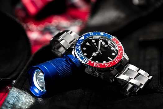 closeup luxury wristwatch for men with black dial blue-red bezel and stainless steel bracelet.