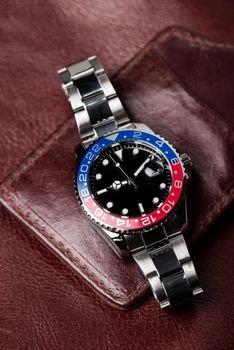 closeup luxury wristwatch for men with black dial blue-red bezel and stainless steel bracelet.