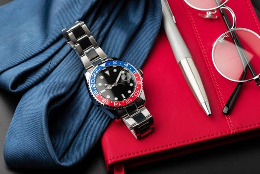 closeup luxury wristwatch for men with black dial blue-red bezel and stainless steel bracelet.