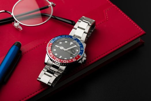 closeup luxury wristwatch for men with black dial blue-red bezel and stainless steel bracelet.
