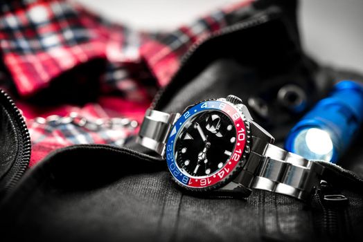 closeup luxury wristwatch for men with black dial blue-red bezel and stainless steel bracelet.