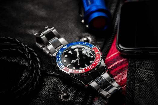 men's accessories, closeup at wristwatch with black dial blue-red bezel and stainless steel bracelet.