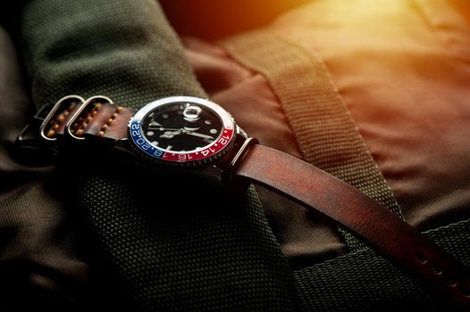 closeup luxury wristwatch for men with black dial blue-red bezel and leather strap. wristwatch with vintage men's objects.