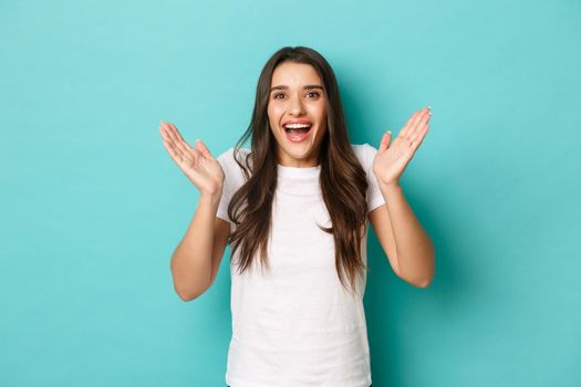 Image of excited attractive girl in white t-shirt, looking fascinated and clapping hands, applause from happiness, standing over blue background.