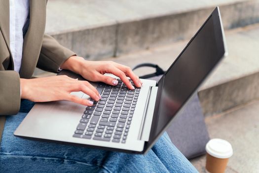 close up of a woman's hands working on her laptop computer sitting on a staircase in the city, concept of business and urban lifestyle, copy space for text