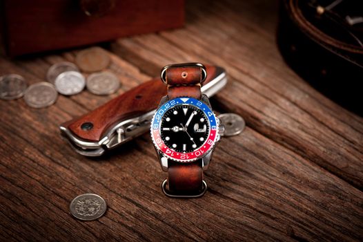 closeup luxury wristwatch for men with black dial blue-red bezel and leather strap.