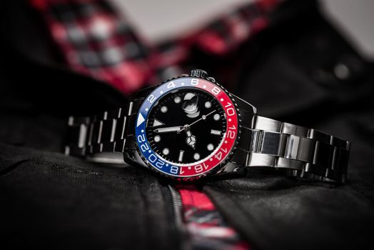 closeup luxury wristwatch for men with black dial blue-red bezel and stainless steel bracelet.