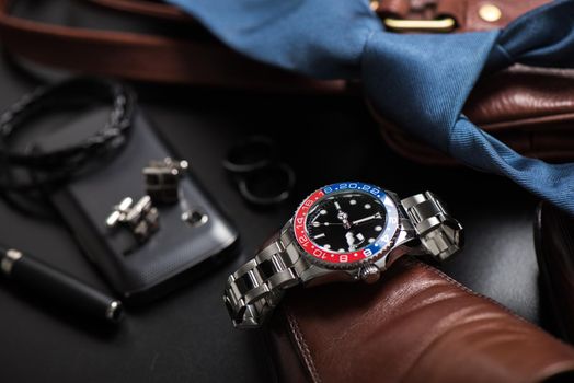 men's accessories, closeup at wristwatch with black dial blue-red bezel and stainless steel bracelet.