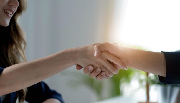 Closeup of unrecognizable happy businesswoman shaking hands with business partner after signing contract during meeting in office..