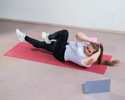 A chubby young woman is watching an online fitness lesson on a laptop. Distance sports training