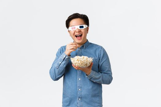Leisure, lifestyle and people concept. Upbeat smiling asian guy in 3d glasses, eating popcorn and enjoying interesting movie, watching streaming service new tv series premier on awesome TV.
