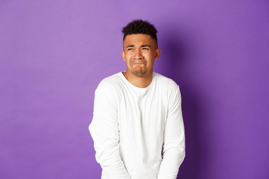 Image of silly guy waiting in line for toilet, grimacing and looking left, need to pee, standing over purple background.