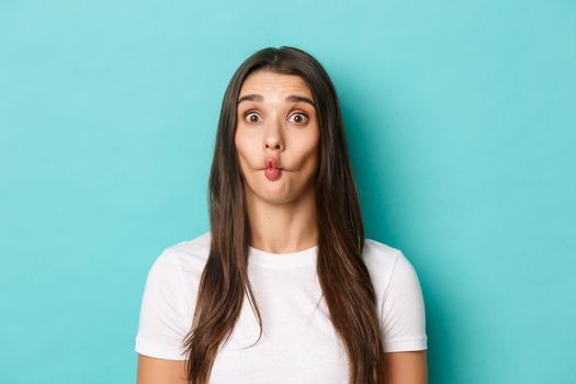 Close-up of silly brunette woman, sucking lips and showing funny faces, standing over blue background.