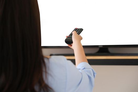 Young woman holding a remote to turn on the TV in the New Normal era where she can't go out of the house, the white space on the TV can be inserted into text or images