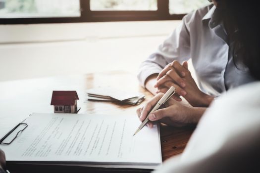 The customer holds a pen and reads the conditions in order to sign a house purchase contract with home insurance documents with the salesperson