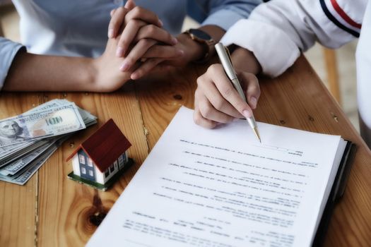 The customer holds a pen and reads the conditions in order to sign a house purchase contract with home insurance documents with the salesperson