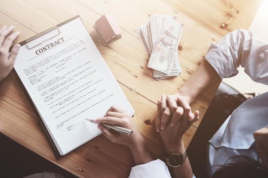 The customer holds a pen and reads the conditions in order to sign a house purchase contract with home insurance documents with the salesperson