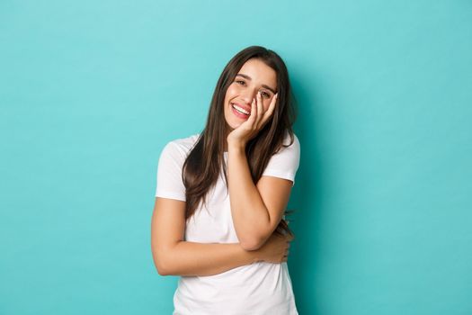Image of happy beautiful woman in white t-shirt, laughing and touching face, standing over blue background.