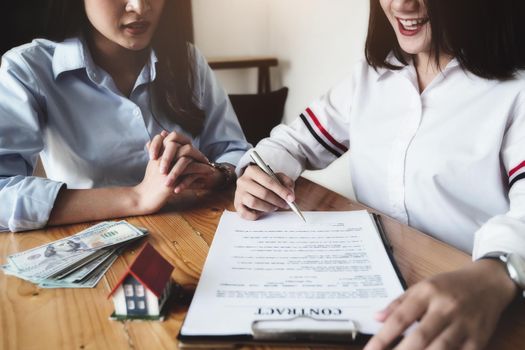 The customer holds a pen and reads the conditions in order to sign a house purchase contract with home insurance documents with the salesperson