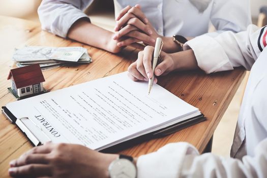 The customer holds a pen and reads the conditions in order to sign a house purchase contract with home insurance documents with the salesperson