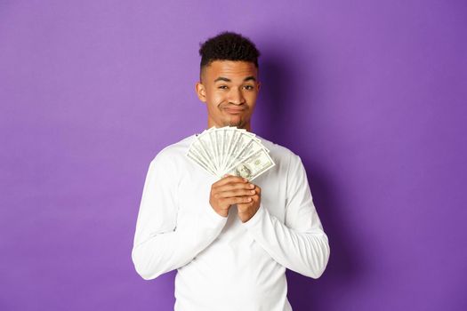 Cheeky african-american guy, winking and showing big sum of money, winning lottery or got loan, standing over purple background.