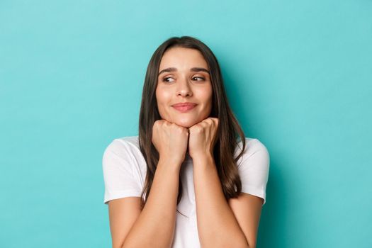 Close-up of romantic and cute brunette girl in white t-shirt, leaning on palms and looking left with admiration, standing over blue background.