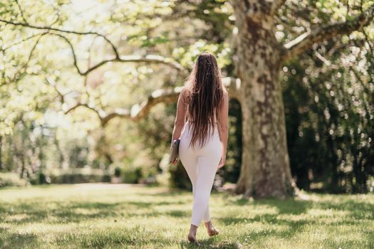 back view of a beautiful woman in a white tracksuit walking in the park with a laptop.