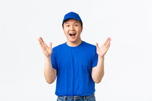 Happy and impressed asian delivery guy in blue courier clap hands, applause glad, praising nice work. Cheerful courier celebrating big event in company, achieve goal, white background.