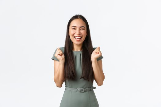 Small business owners, women entrepreneurs concept. Excited happy asian woman in dress, businesswoman winning or achieve goal, fist pump as celebrating victory, triumphing over white background.