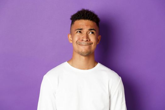 Close-up of troubled african-america man making choice, looking at upper right corner and thinking, standing indecisive over purple background.