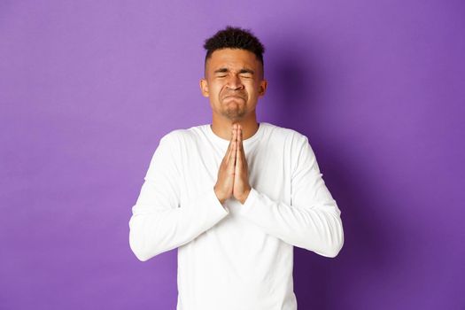 Image of desperate african-american guy pleading to God, holding hands in pray and begging for something, making wish, standing worried and asking for help.