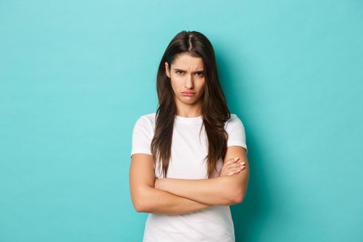 Image of upset sulking girl, feeling offended or jealous, cross arms chest and frowning angry, standing over blue background.