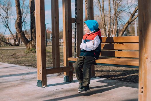 The offended boy is sitting on a lifestyle bench . Childish grievances. Childish anger. An article about children's emotions. An article about the psychology of children. Transitional age