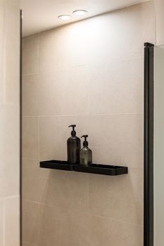 Bottles of gel and shampoo in modern shower with beige wall. Minimalist bathroom interior.