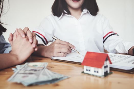 The customer holds a pen and reads the conditions in order to sign a house purchase contract with home insurance documents with the salesperson