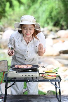 Happy female tourist grilled meat on portable camping stove. Adventure, travel and camping concept.