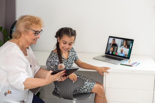 Happy grandmother and her granddaughter having video chat via laptop together at home.