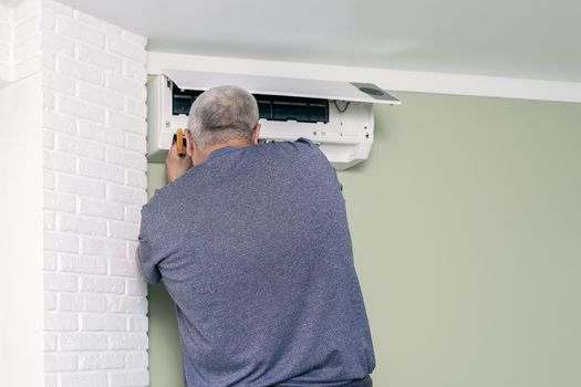 master man repairing indoor unit of home air conditioner using screwdriver