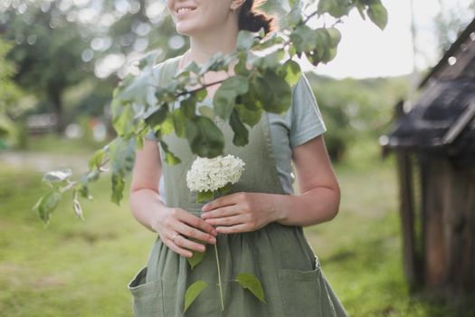 young woman in apron holding flowers in the garden in summer. gardening and profession concept