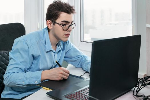 Young male graphic designer uses a graphics tablet to do his work at the table