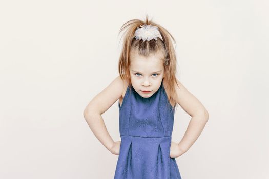 portrait of grumpy little cute girl in blue dress. hands to the sides. children's emotions