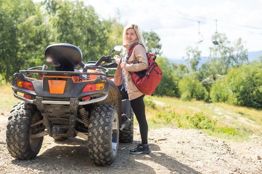 Smiling happy woman riding quad bike on a sunny day, against blue sky. Low angle shot. Freedom, happiness, nature concept.