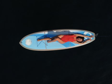 Young attractive brunette woman in red swimsuit, swimming on kayak around volcanic rocks, like in Iceland. Back view. Christmas holiday vacation and travel concept.