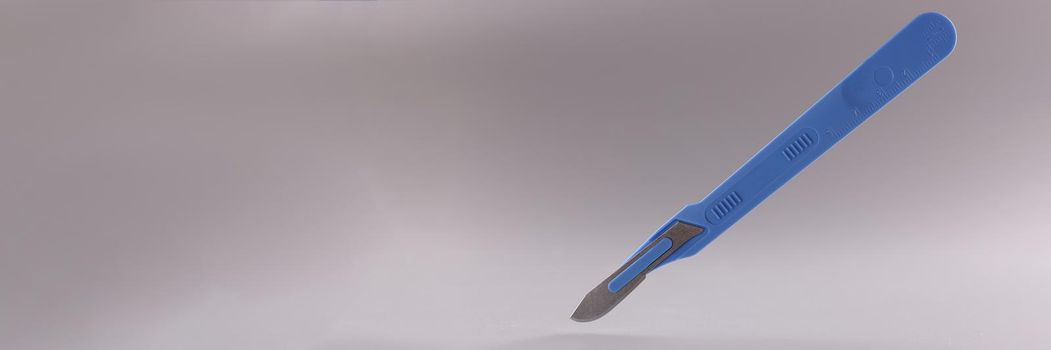 Medical scalpel with blue handle on gray background.