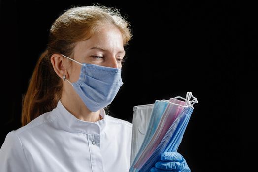 the doctor holds several masks of different colors in his hands. A nurse wearing a mask and medical gloves counts the protective disposable masks on a black background. Isolate