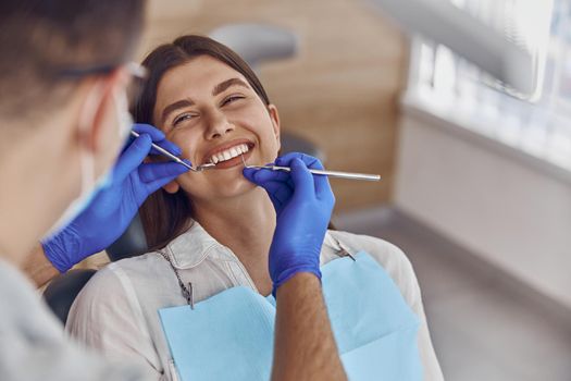 Professional doctor is checking woman's teeth in light modern dental clinic