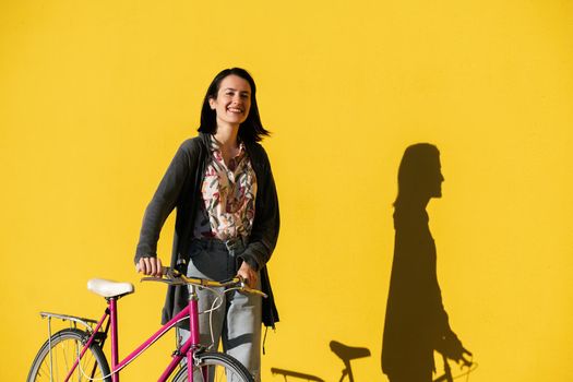happy young girl walking with a pink retro bike in front of a colorful yellow wall, concept of active lifestyle and sustainable mobility, copy space for text